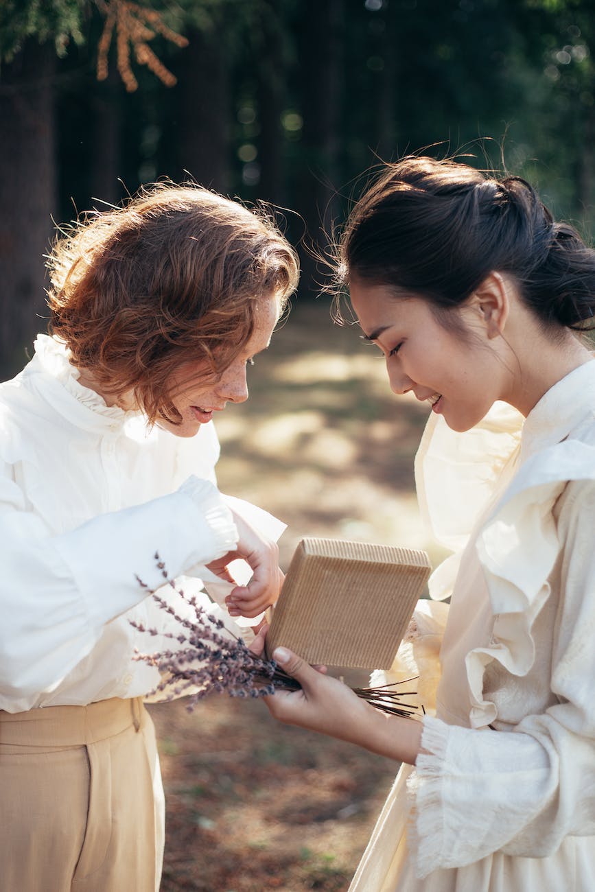 smiling women in old fashioned clothing looking at gift in park