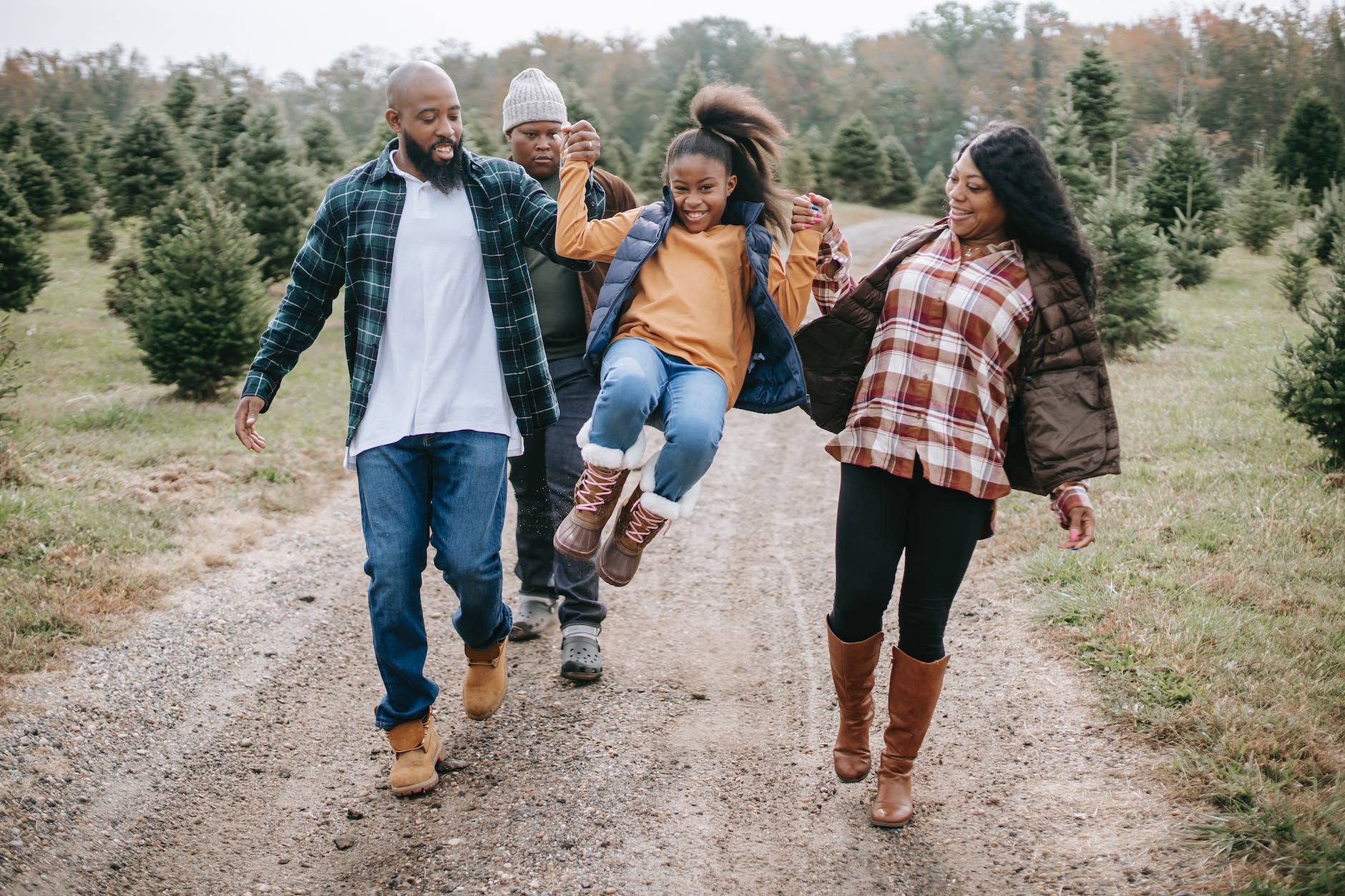 ethnic parents raising cheerful girl on tree farm roadway